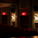 Theater auditorium showing emergency lighting systems and exit signs for fire safety compliance